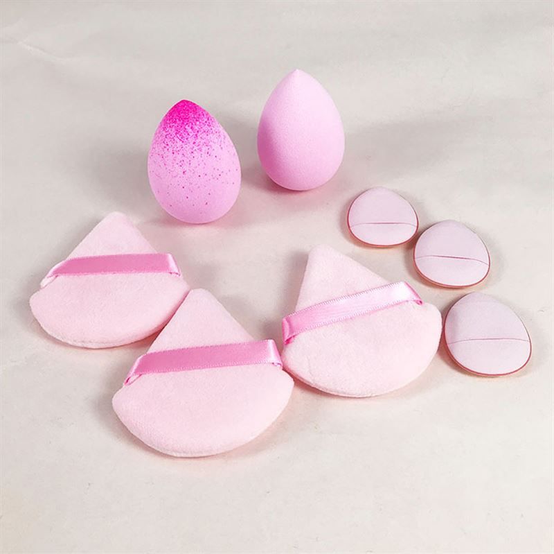 Éponges de maquillage de formes et couleurs variées. Éponges en forme de goutte et triangulaires avec des rubans. Plusieurs éponges sont visibles.