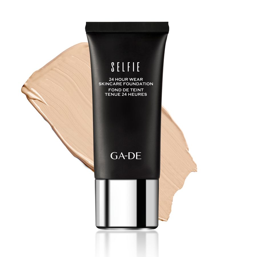 Tube noir avec logo GA-DE et inscription "SELFIE 24 Hour Wear Skincare Foundation". À côté, une traînée de fond de teint beige clair.
