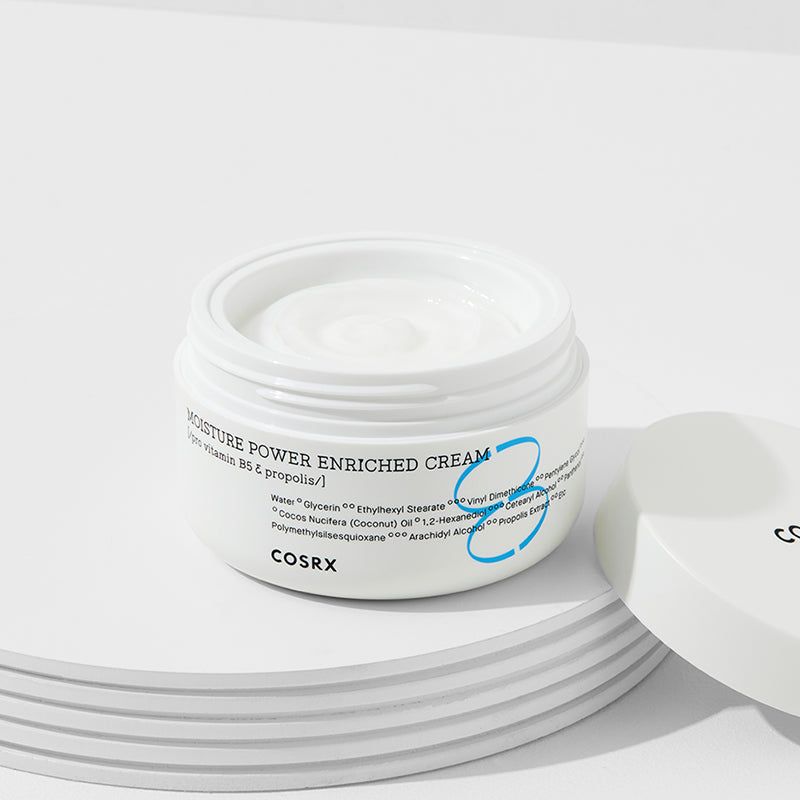 Open crème pot op wit oppervlak. Opschrift: MOISTURE POWER ENRICHED CREAM, COSRX. Deksel ernaast.