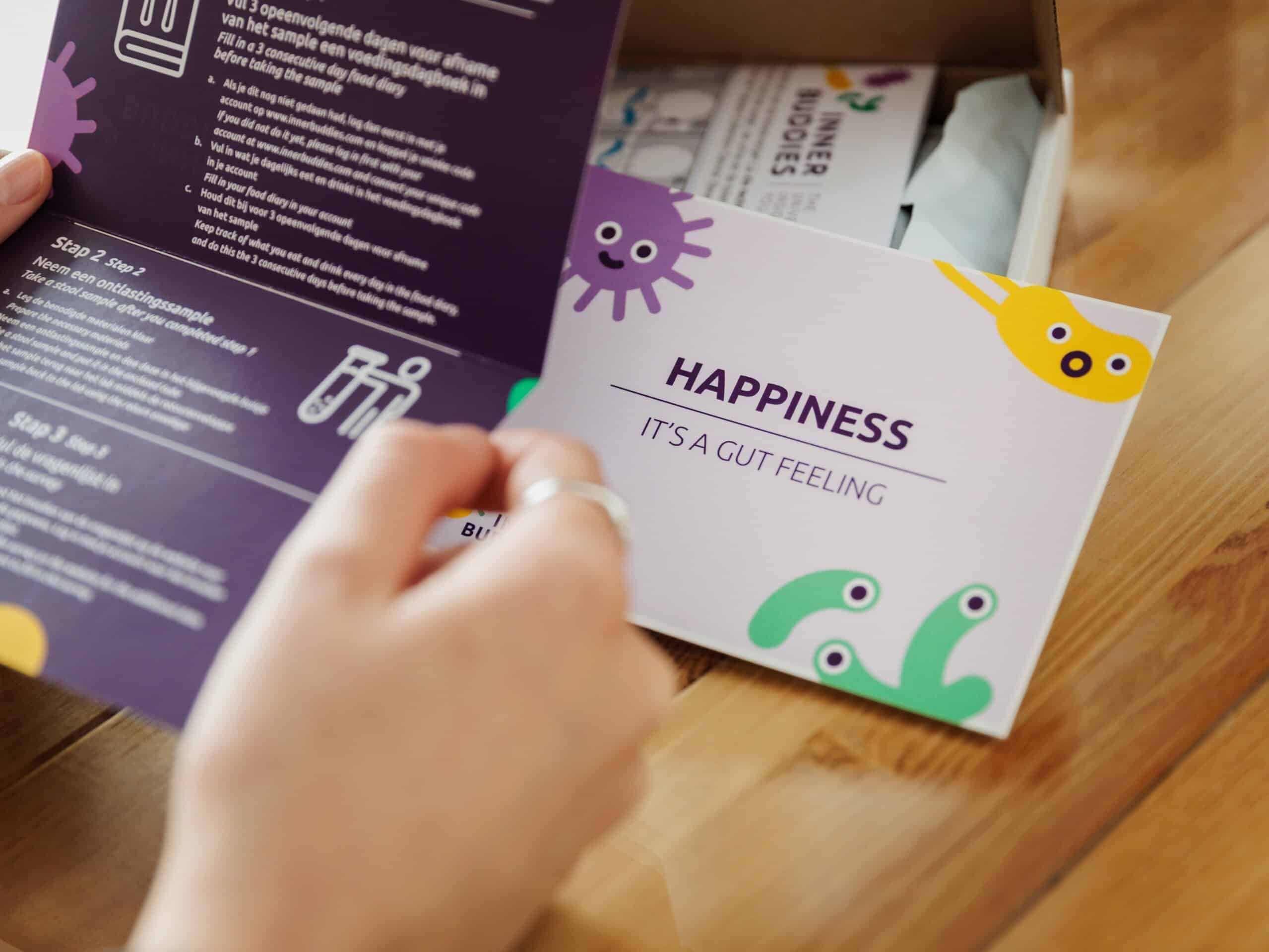 Persoon opent een brochure met instructies en een kaart met 'Happiness - It's a Gut Feeling'.