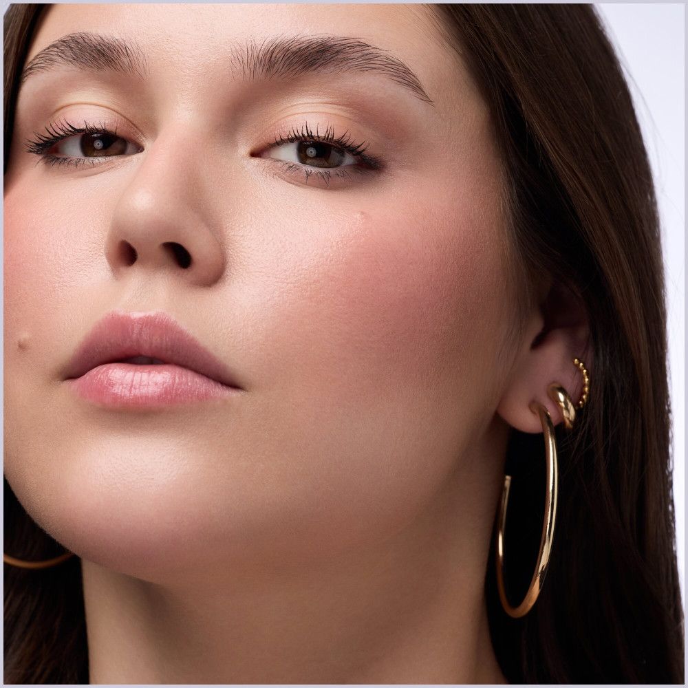 Gros plan sur une femme à la peau bronzée. Fard à joues sur les joues. Boucles d'oreilles dorées.