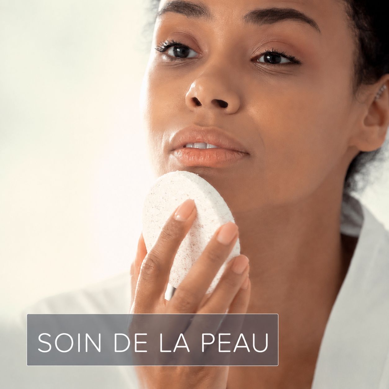 Une femme utilise une éponge ronde et blanche pour le soin de la peau.