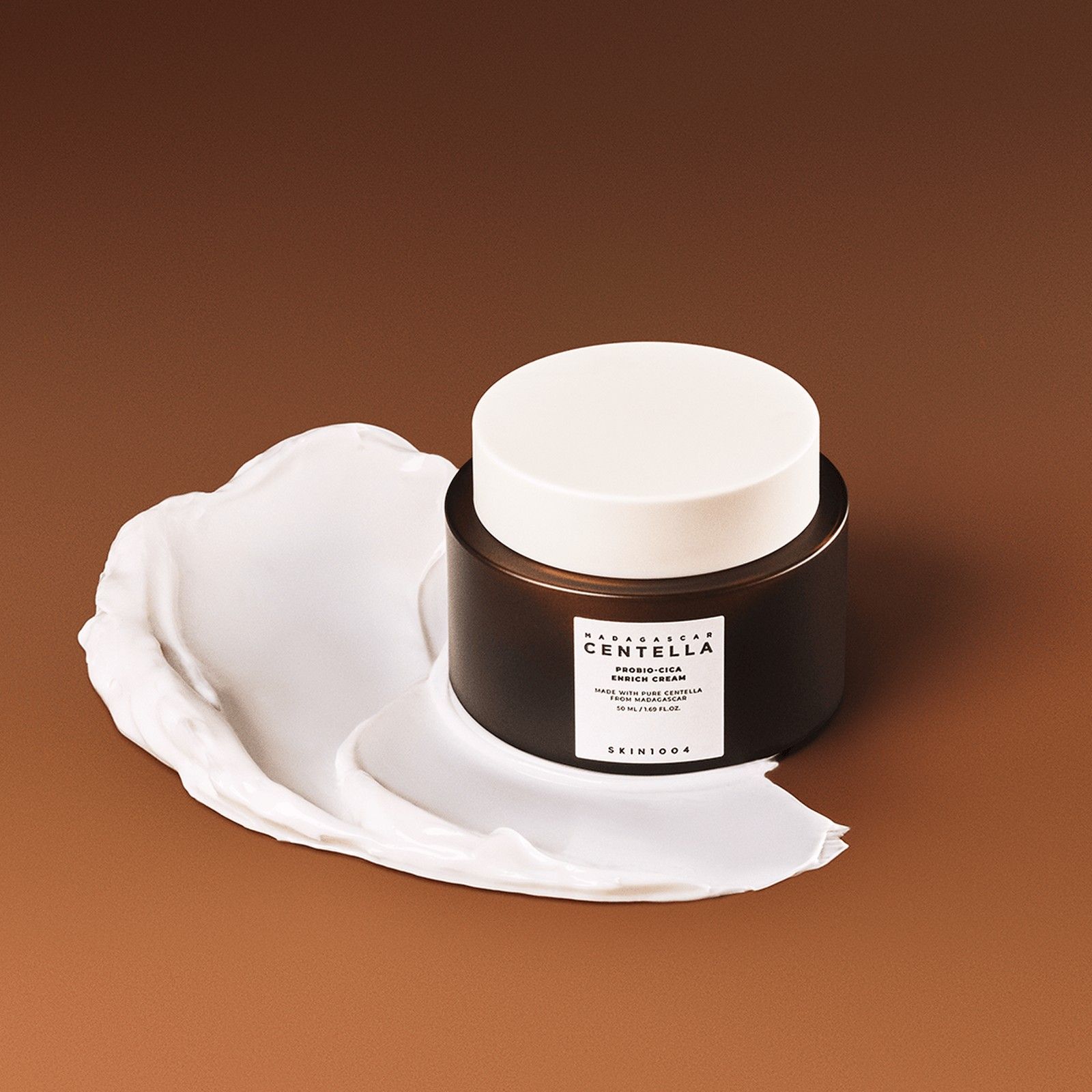SKIN1004 Madagascar Centella Probio-Cica Enrich Cream met een veeg crème op bruine achtergrond.