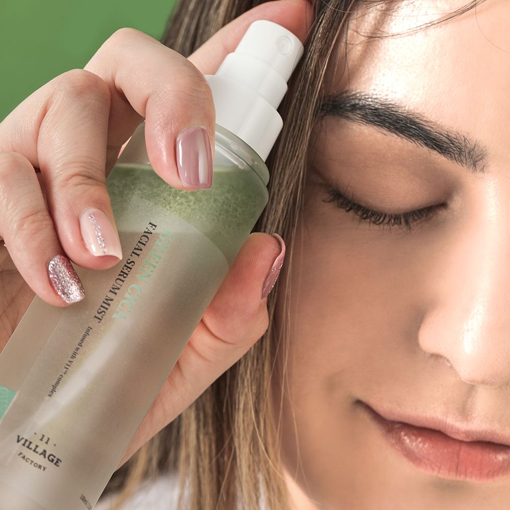 Persoon spuit serum op haar gezicht. Fles met groene band en witte dop. Opschrift: Green Cica Facial Serum Mist.
