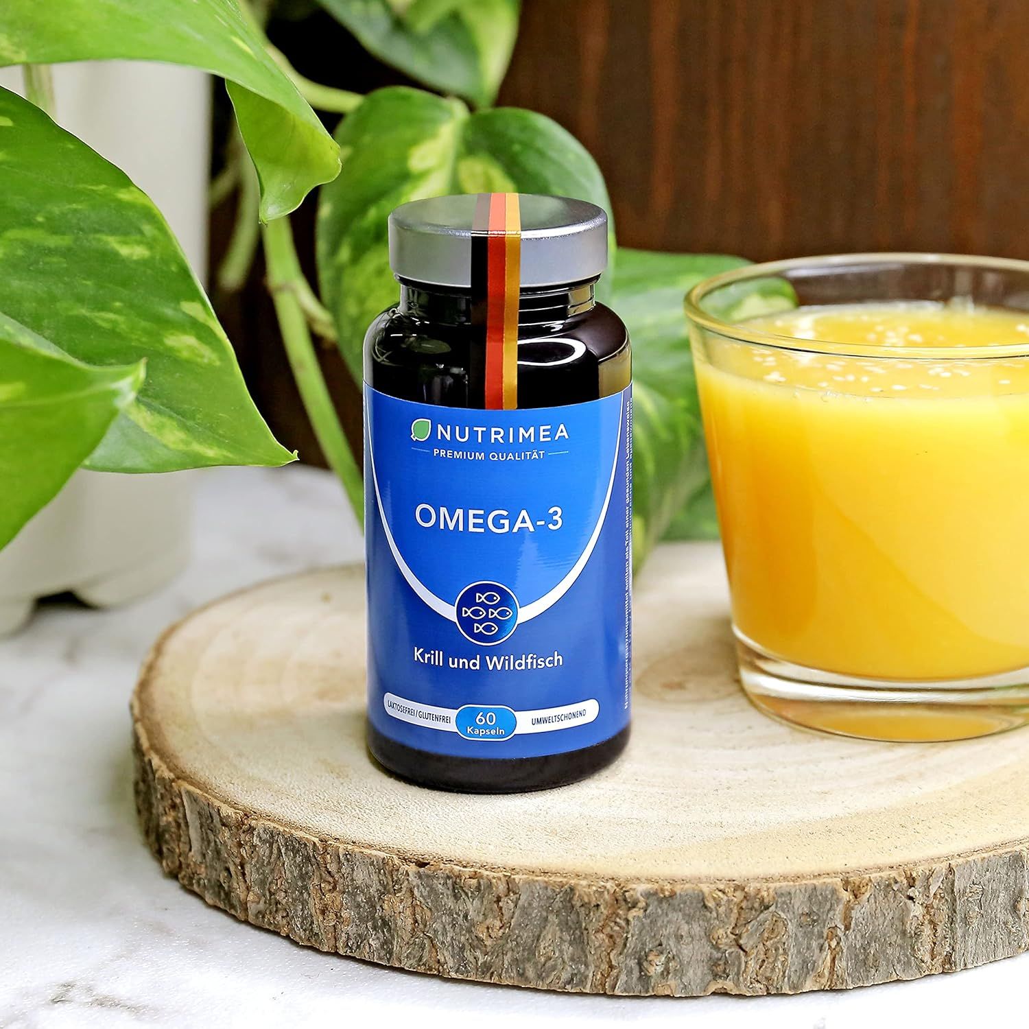 Fles Omega-3 capsules op houten plank. Glas sinaasappelsap ernaast. Groene achtergrond.