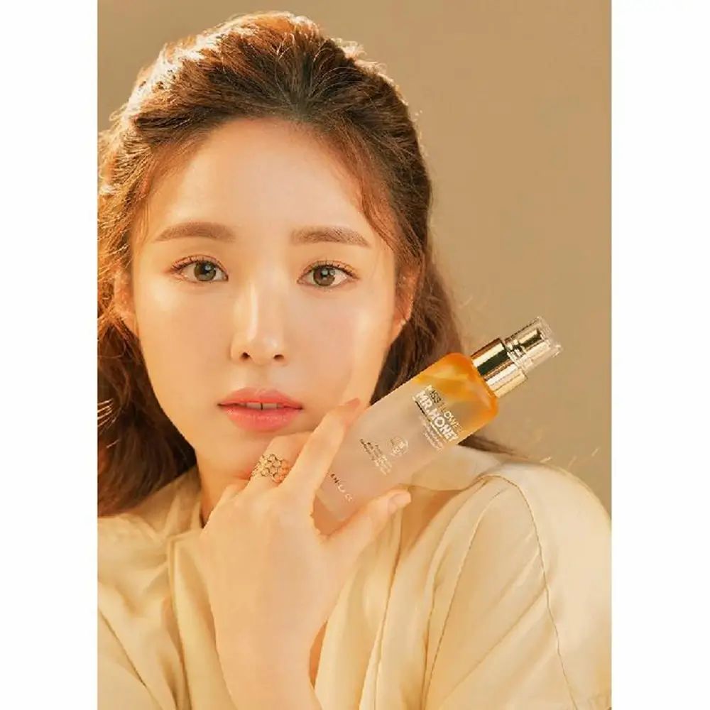 Vrouw houdt gezichtsspray vast. Gouden dop, gelige vloeistof. Opschrift: Miss Flower & Mr. Honey.