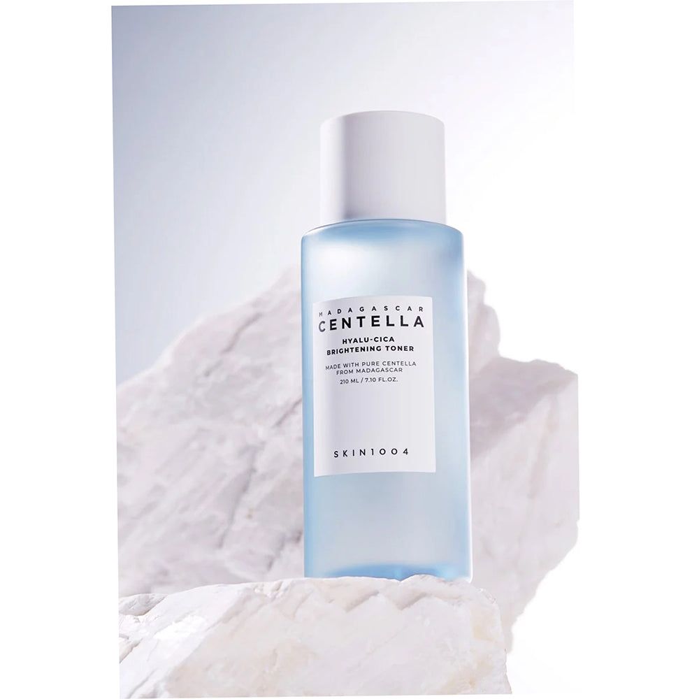 Blauw-transparante fles op een steen. Opschrift: MADAGASCAR CENTELLA, HYALU-CICA BRIGHTENING TONER, SKIN1004.