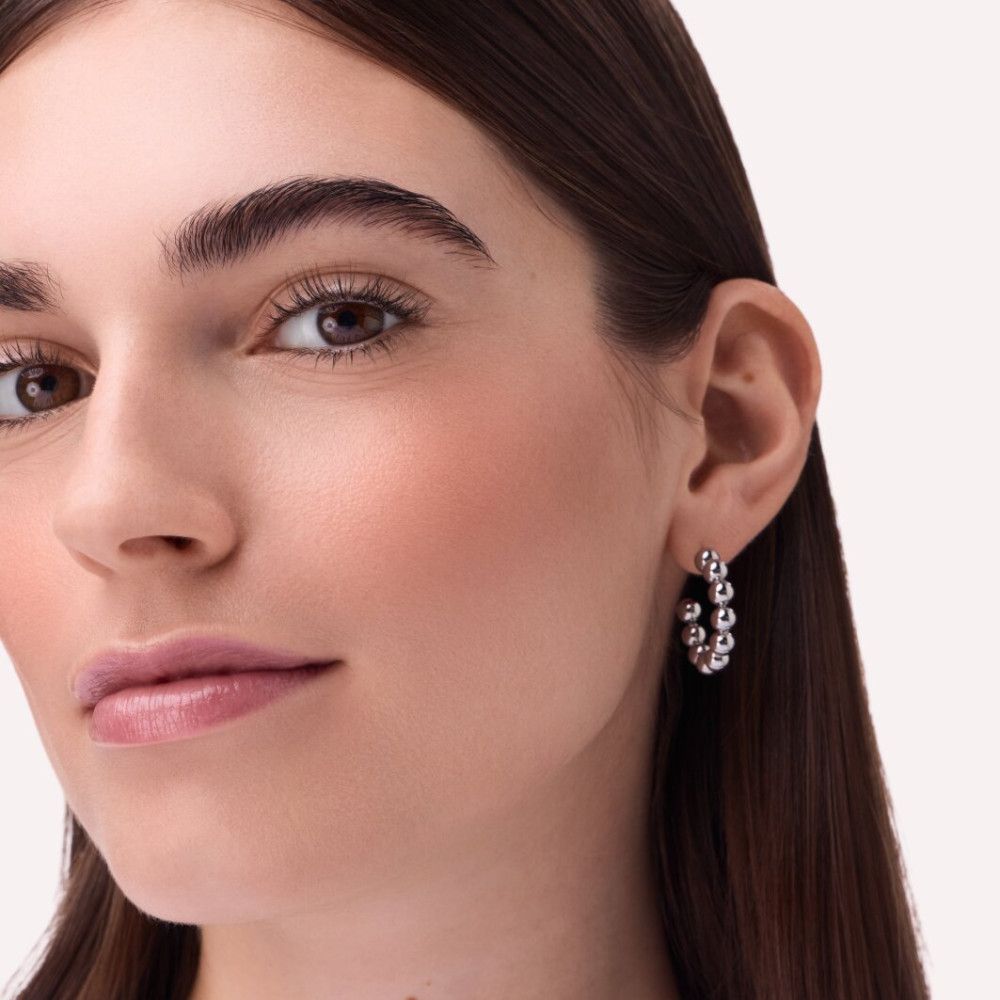 Gros plan d'un visage avec fard à joues sur les joues. La personne porte des boucles d'oreilles.