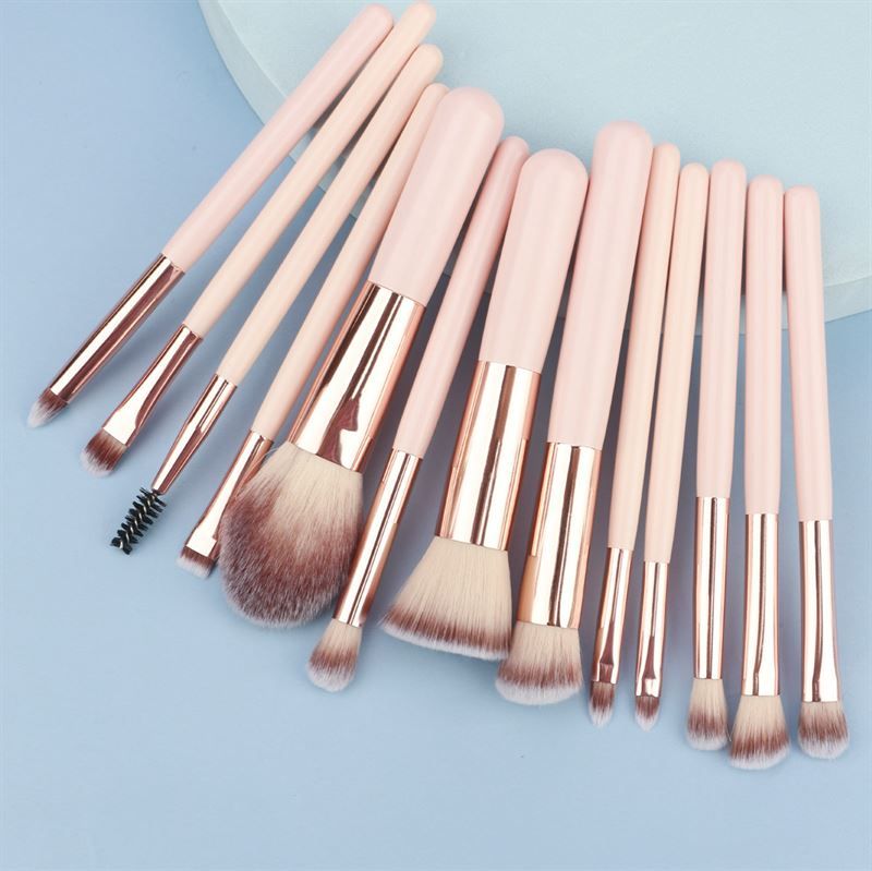 Ensemble de pinceaux de maquillage. Manches roses, viroles dorées, différentes têtes. Sur fond bleu.