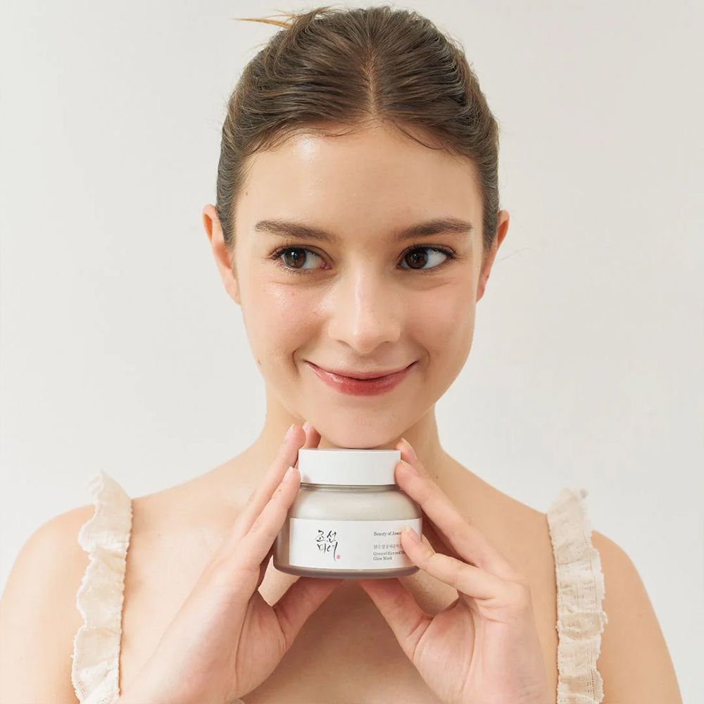 Jonge vrouw die een pot BEAUTY OF JOSEON Ground Rice and Honey Glow Mask vasthoudt.