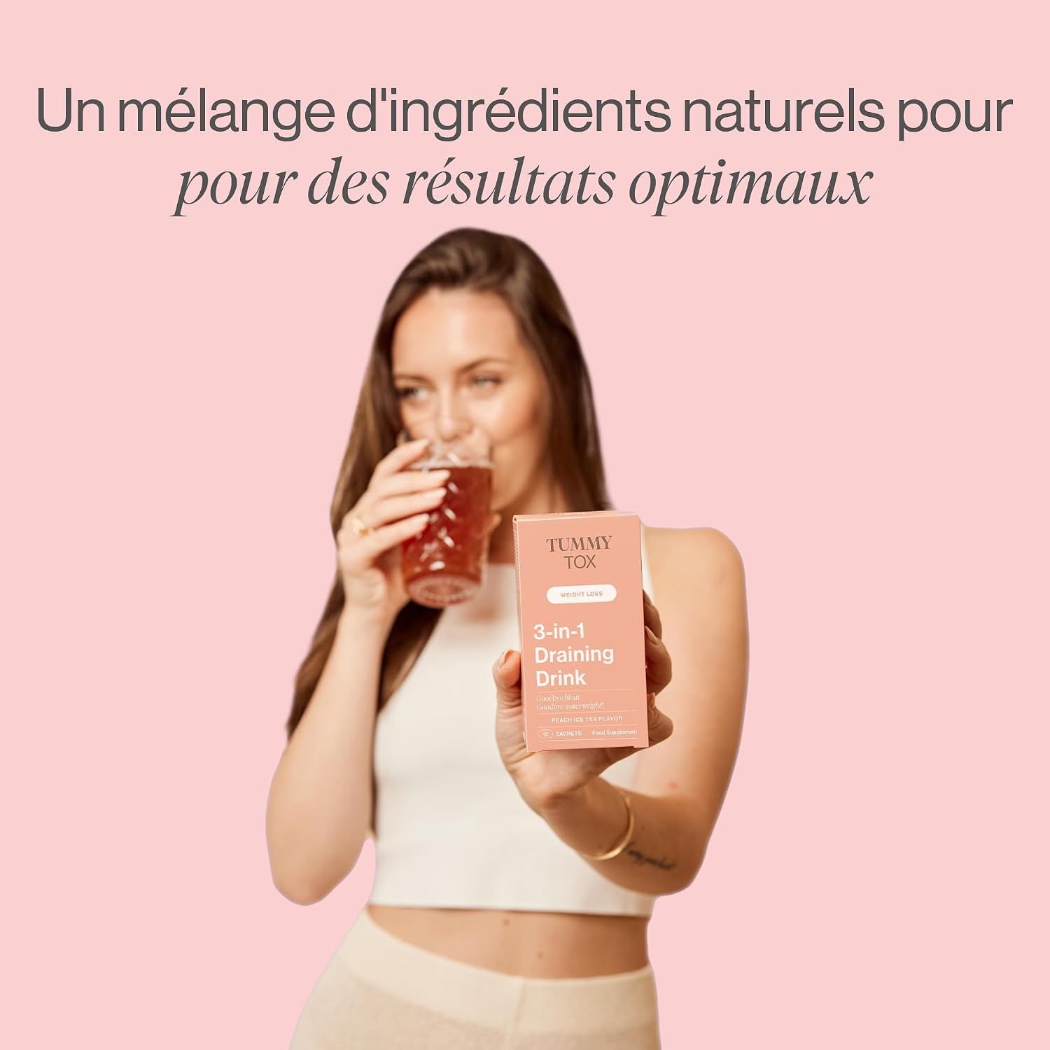 Femme tenant une boîte de Tummy Tox 3-en-1 Draining Drink et buvant un verre.