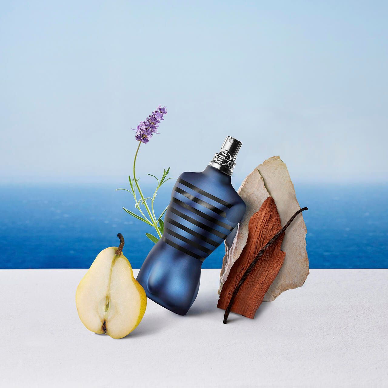 Blauwe torso-vormige fles, omringd door lavendel, peer, hout en steen. Achtergrond: zee.