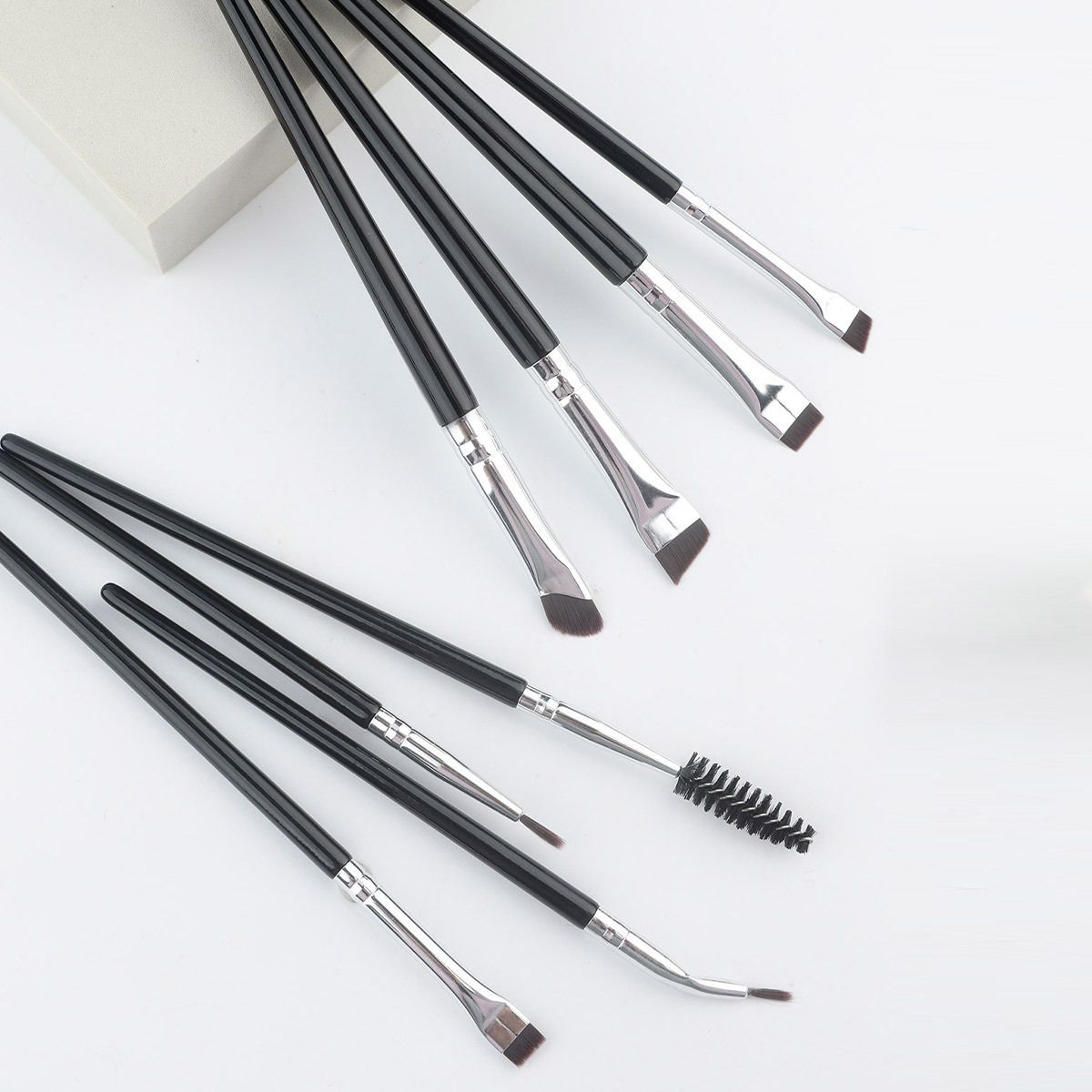 Ensemble de huit pinceaux de maquillage noirs avec viroles argentées et différentes extrémités, y compris des brosses biseautées et des brosses.