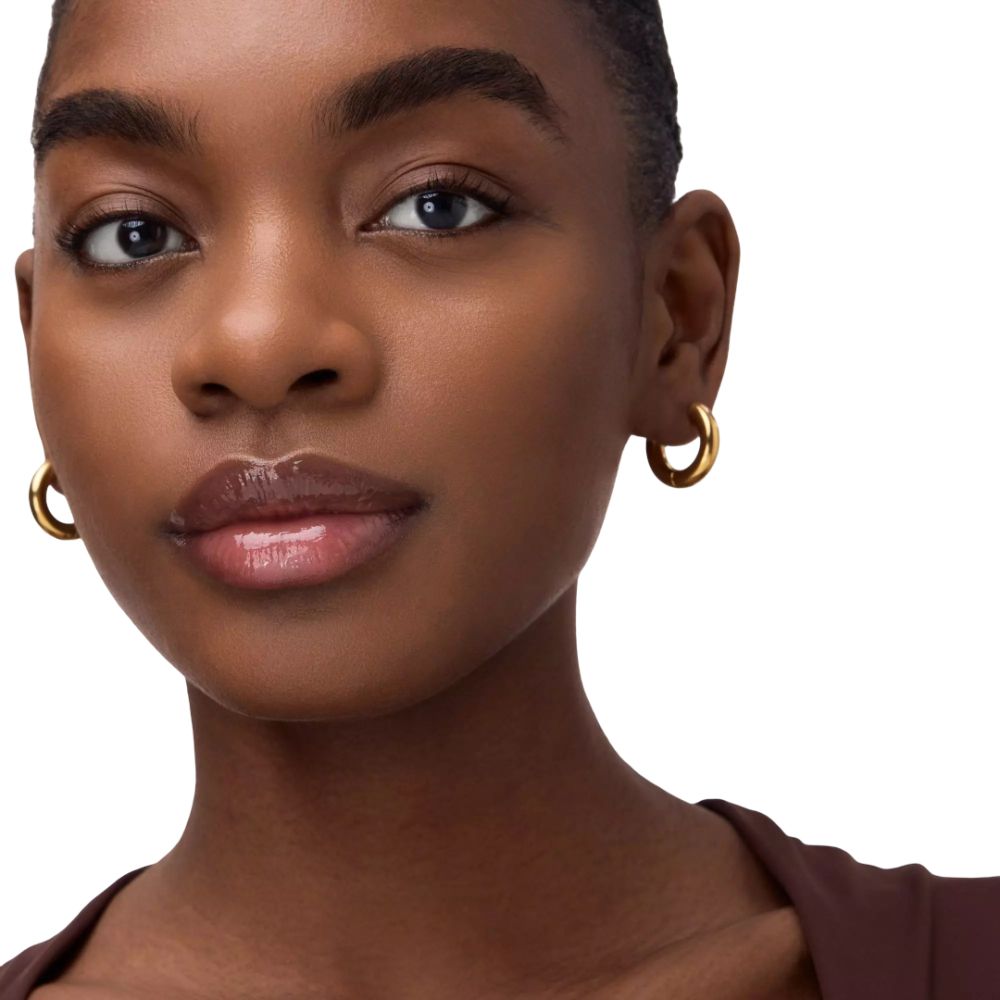 Portret van een vrouw met een donkere huid en gouden oorringen. Ze kijkt in de camera.