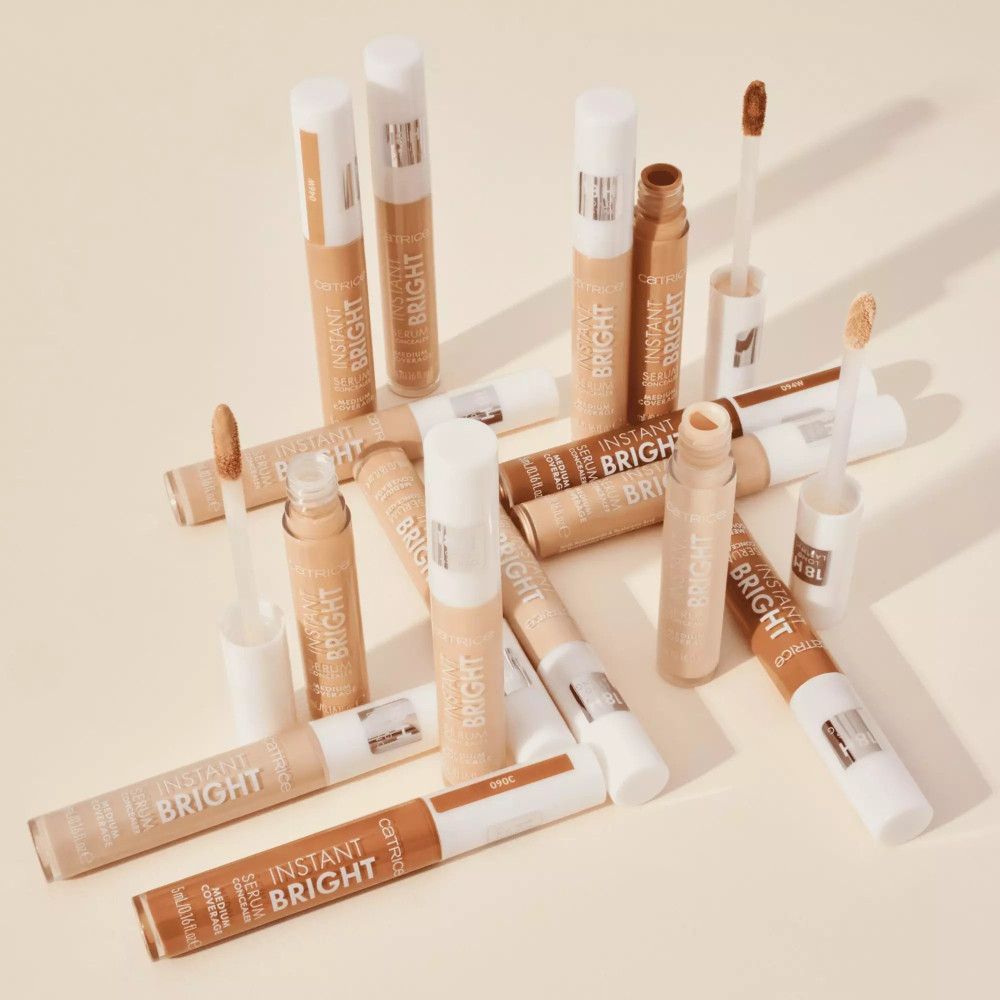 Plusieurs tubes et applicateurs de correcteur sont dispersés. Inscription : INSTANT BRIGHT, SERUM CONCEALER.
