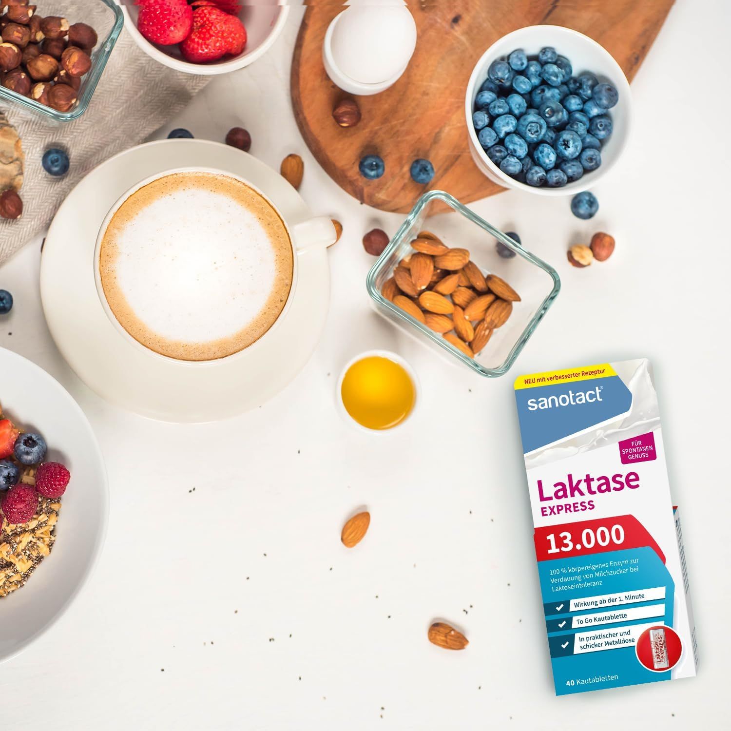 Verpakking sanotact Laktase 13.000 EXPRESS op witte tafel. Omringd door voedsel: koffie, bessen, noten, eieren, amandelen.