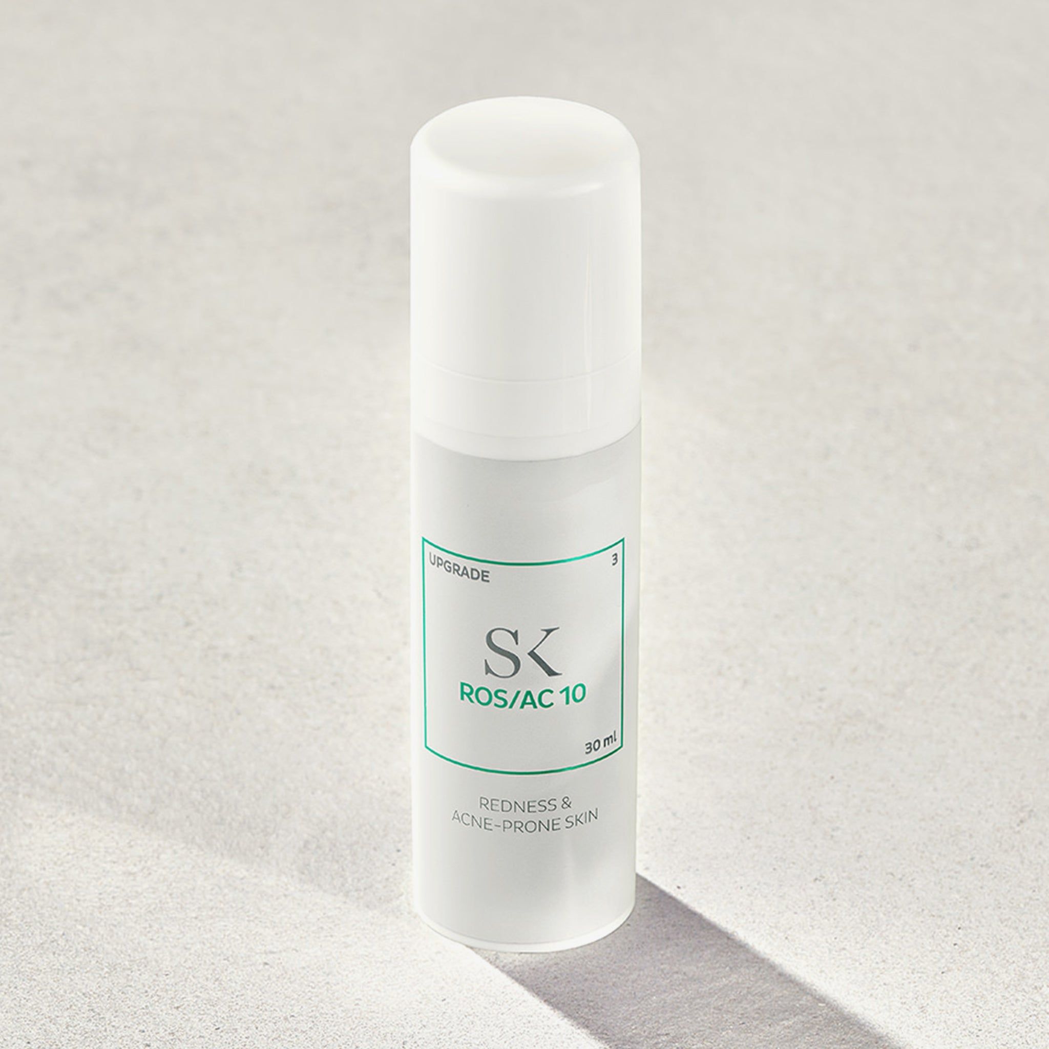 Flacon blanc avec étiquette verte. Inscription : SK ROS/AC 10, 30 ml. Texte : Redness & Acne-Prone Skin. Ombre.