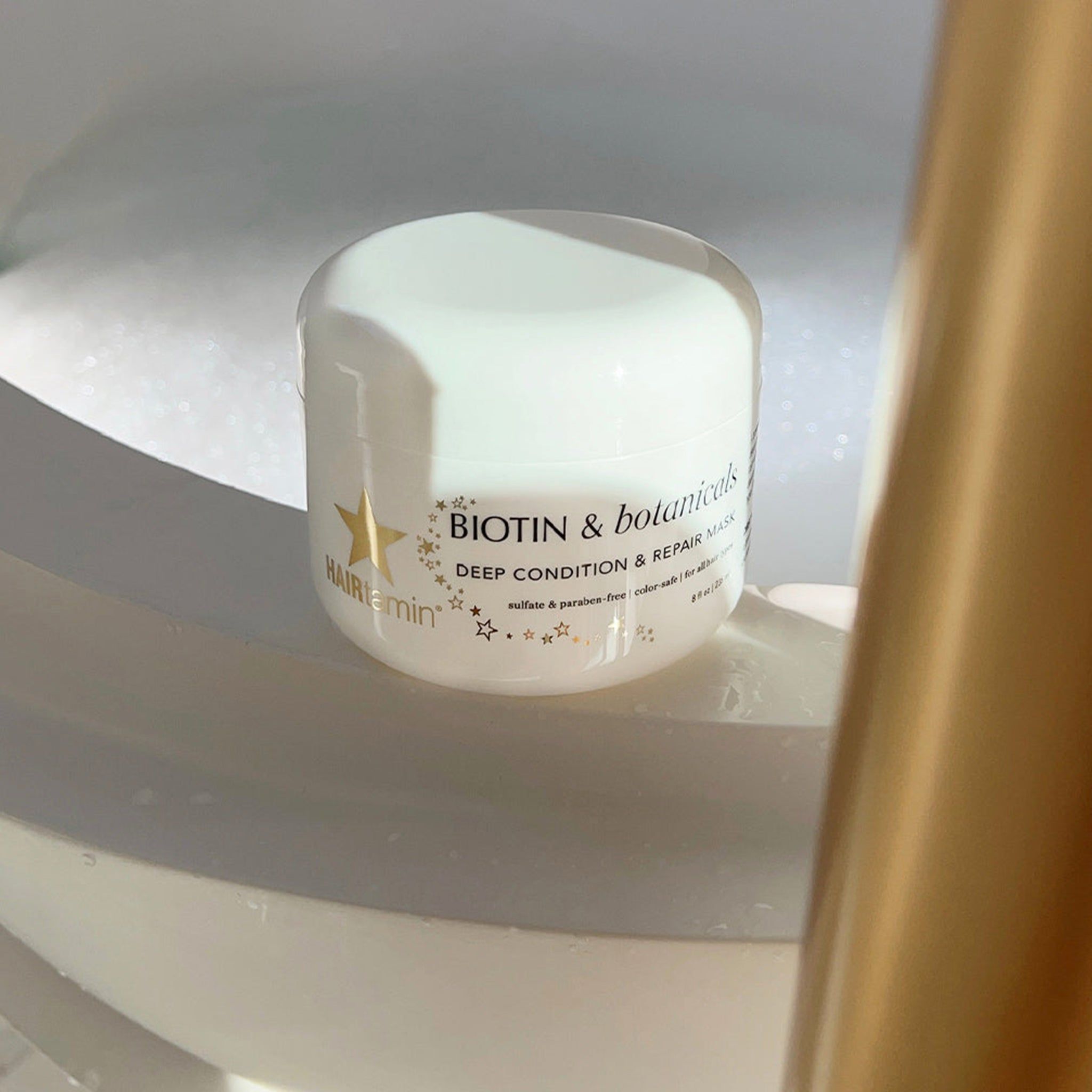 Pot blanc de masque capillaire dans une baignoire. Texte: BIOTIN & botanicals DEEP CONDITION & REPAIR MASK.
