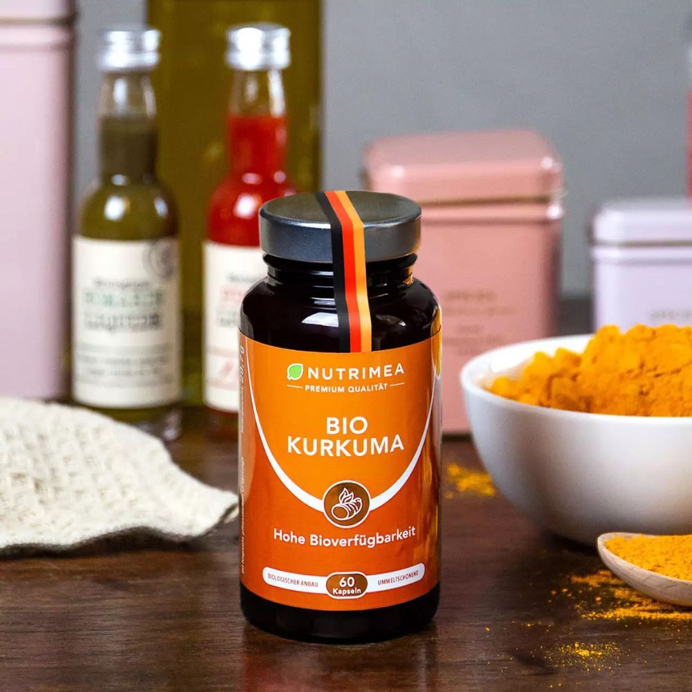 Flacon de produit sur une table, entouré d'ingrédients et d'accessoires. Inscription : BIO KURKUMA, 60 gélules.