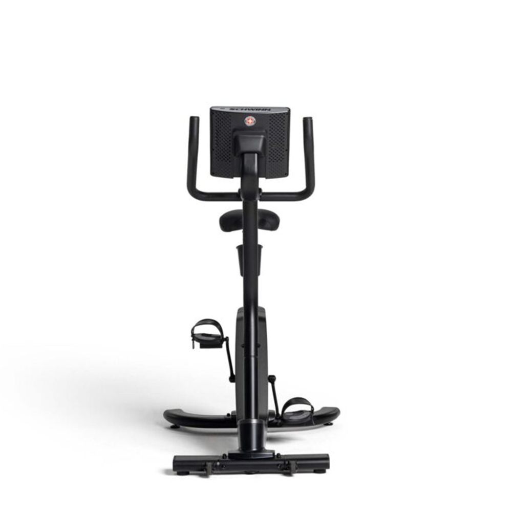Vélo d'appartement noir, vue de face. Console, guidon, pédales et pieds visibles.