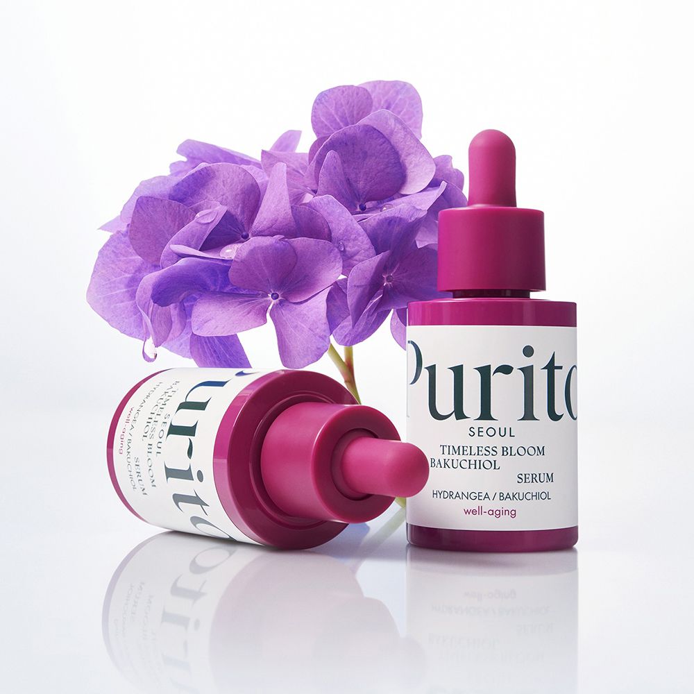 Twee PURITO Timeless Bloom Bakuchiol Serum flesjes. Paarse bloemen op witte achtergrond.