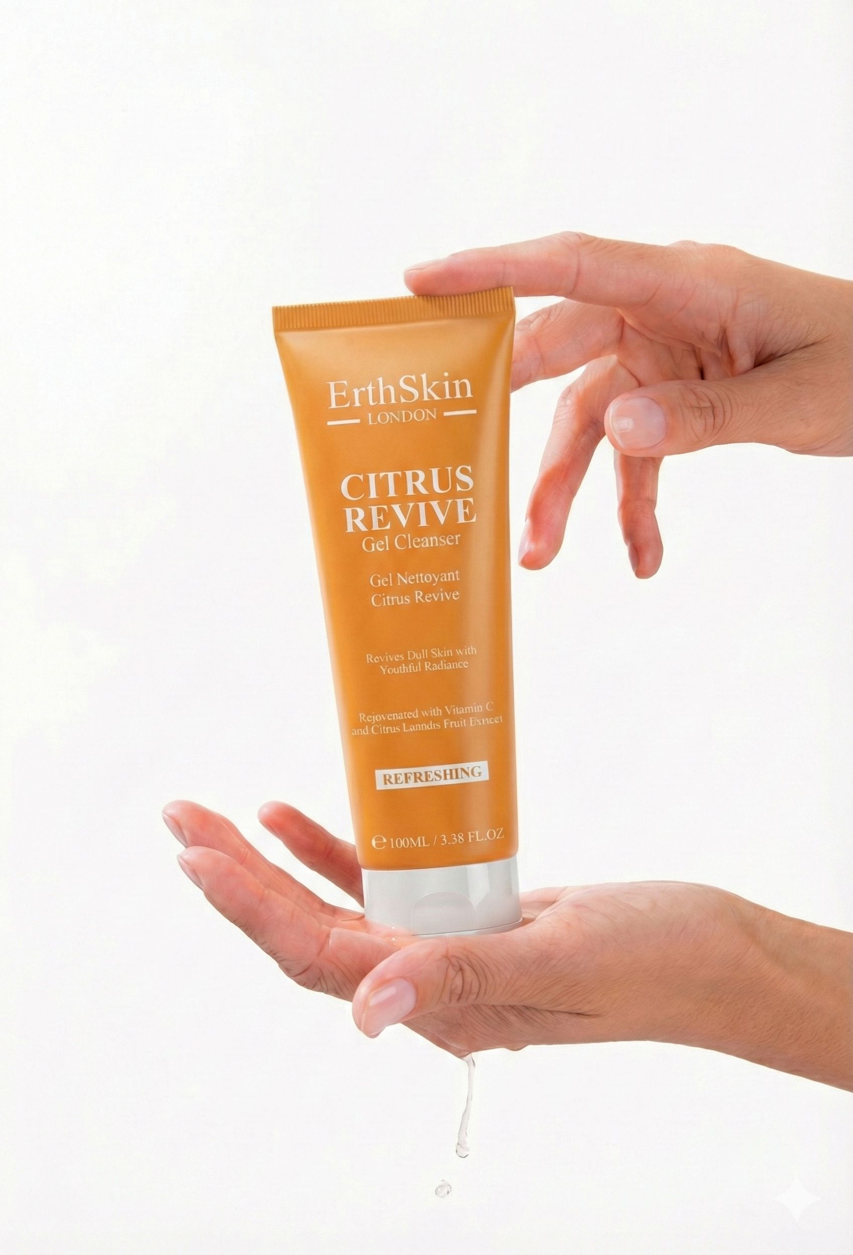 Mains tenant un tube orange. Inscription : ErthSkin London CITRUS REVIVE Gel Cleanser. Goutte de liquide.