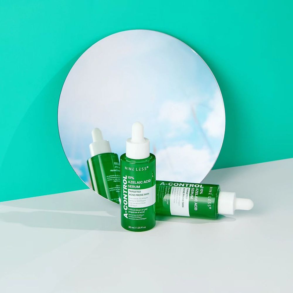 Twee groene flessen met witte druppelaar voor een spiegel. Opschrift: A-Control, 10% Azelaïnezuur Serum.