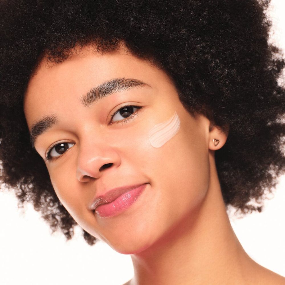 Visage d'une personne avec produit sur la peau. Couleur du produit : rose.