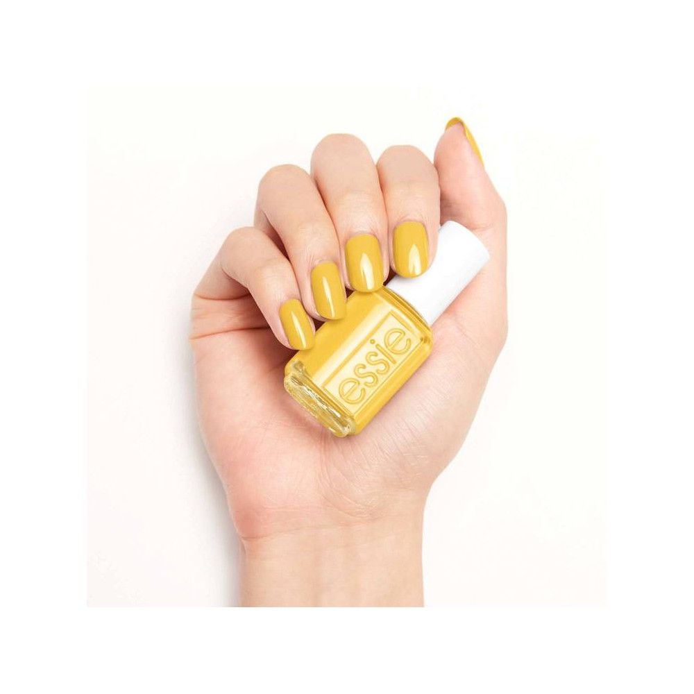 Hand met gelakte nagels en nagellakflesje. Gele nagellak. Flesje met witte dop, opschrift 'essie'.