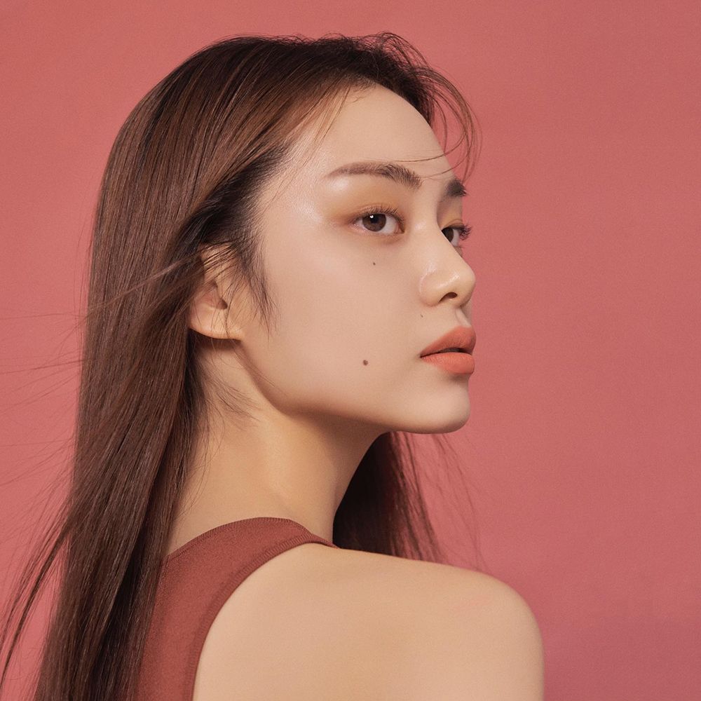 Portret van een vrouw met lippenstift. Ze draagt een rode top. Roze achtergrond. Lippenstiftkleur passend bij de huidskleur.