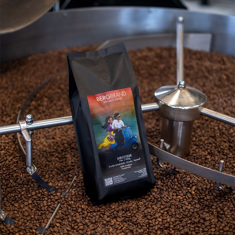 Zwarte zak met BERGBRAND-logo en illustratie. Koffiebonen op de achtergrond. Tekst: Spritztour, Specialty Coffee.