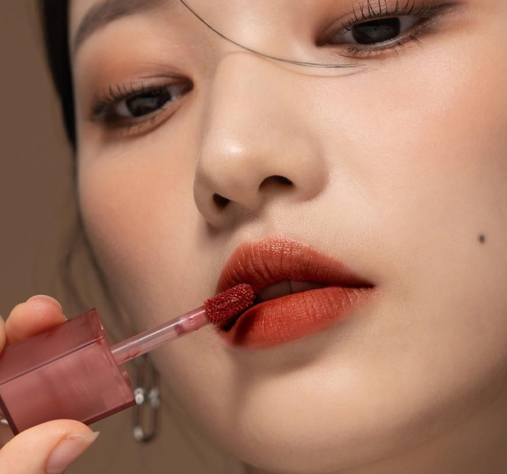 Gros plan d'une femme appliquant du gloss. L'applicateur est visible. Les lèvres sont couvertes de gloss.