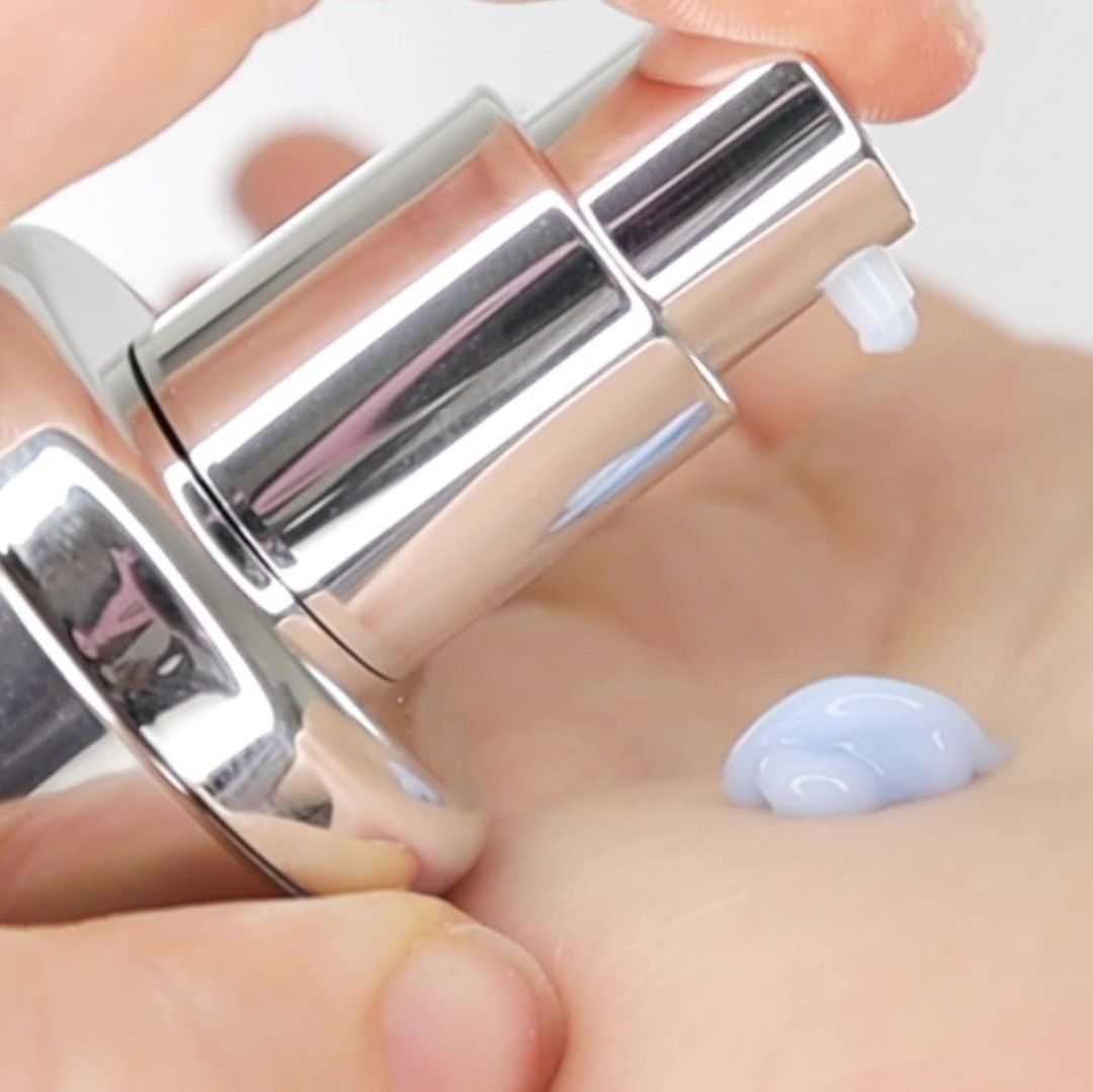 Close-up van een hand die een kleine hoeveelheid blauw serum uit een verstuiver afgeeft. Serum op de handpalm.