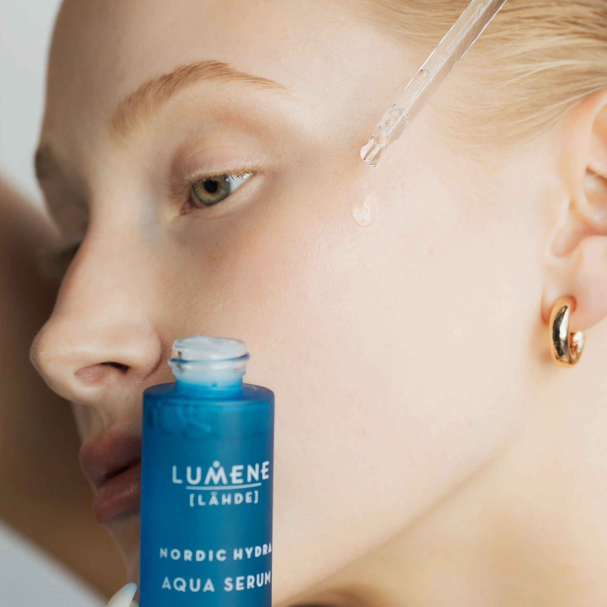Femme avec flacon et pipette de sérum. Le sérum est appliqué sur la peau. Inscription : Lumene [LAHDE] Nordic Hydra Aqua Serum.
