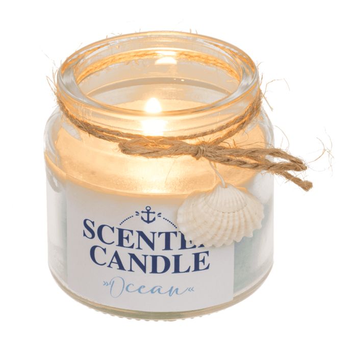 Bougie parfumée allumée en verre. Cire bleue, étiquette avec ancre et texte "SCENTED CANDLE Ocean". Décorée d'un coquillage.
