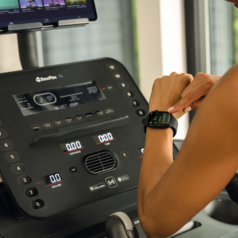 Close-up van de console van een loopband. Een persoon tikt op een smartwatch.