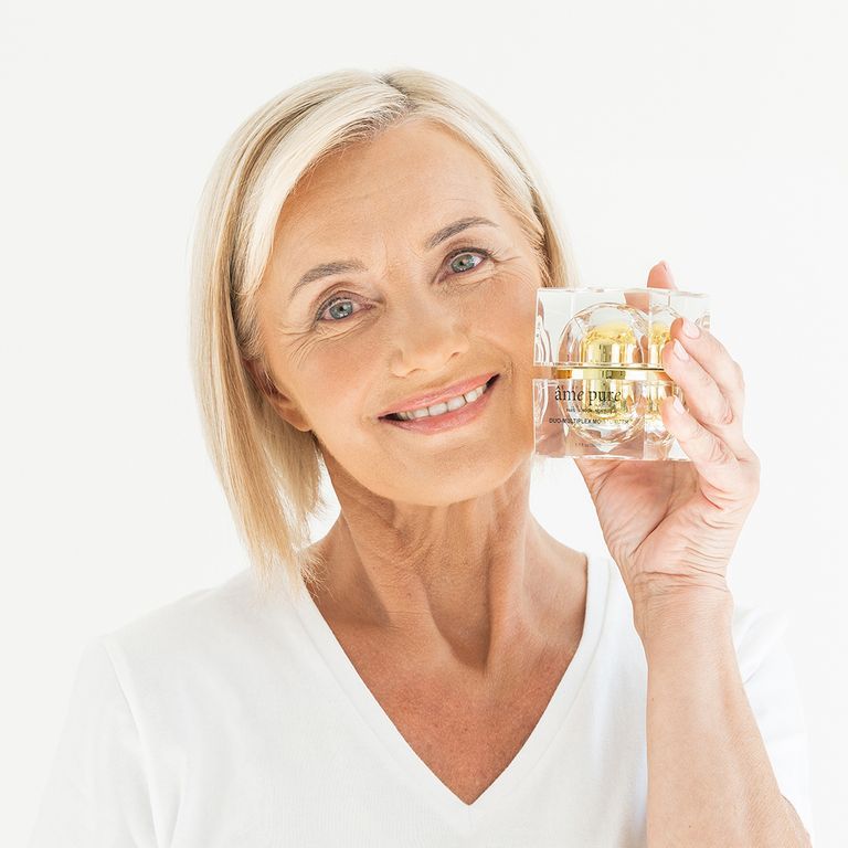 Een lachende vrouw houdt een âme pure Duo-Multiplex Moisturizer voor haar gezicht. Ze draagt een wit T-shirt.