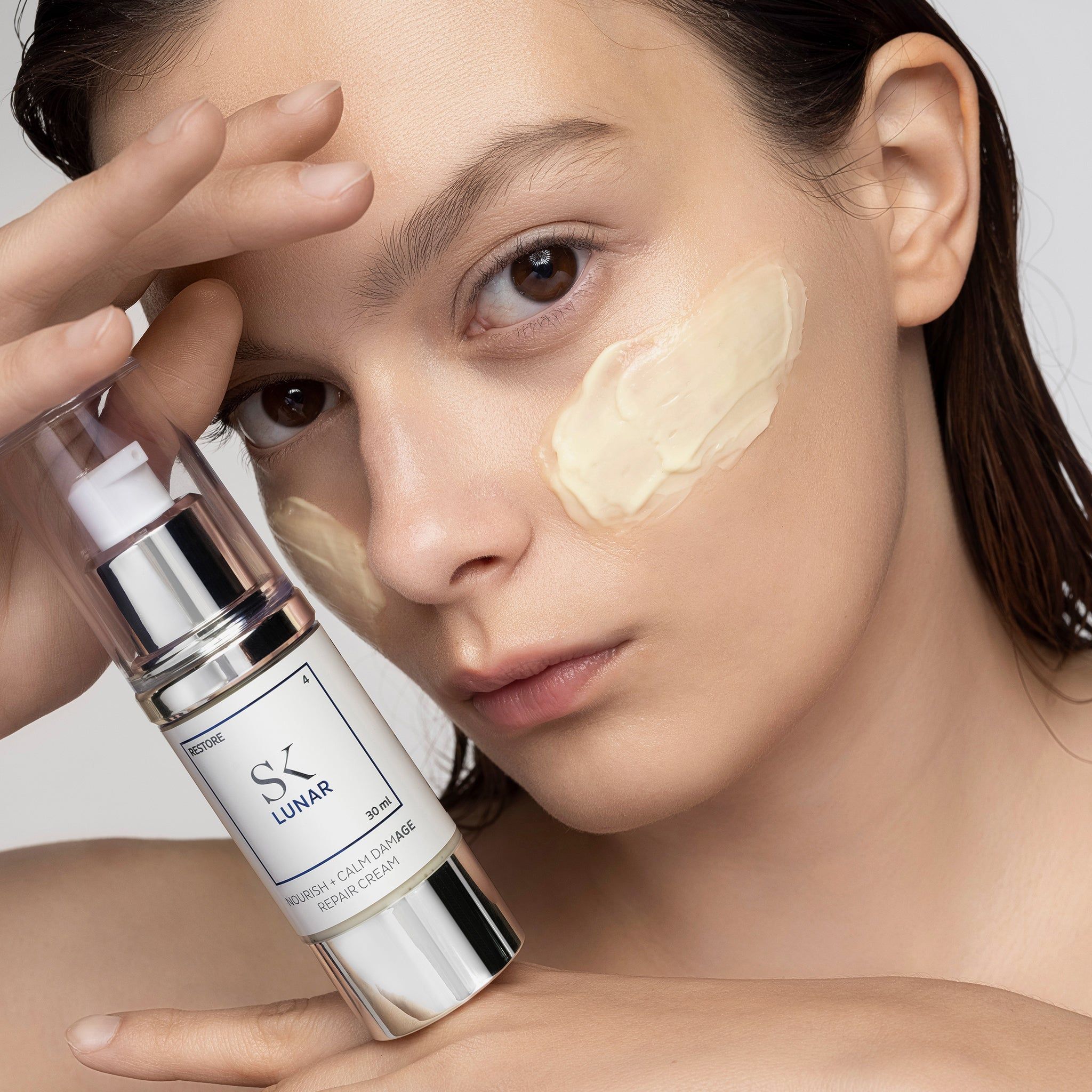Femme avec crème sur le visage. Flacon de crème en main. Inscription : SK Lunar, 30 ml.