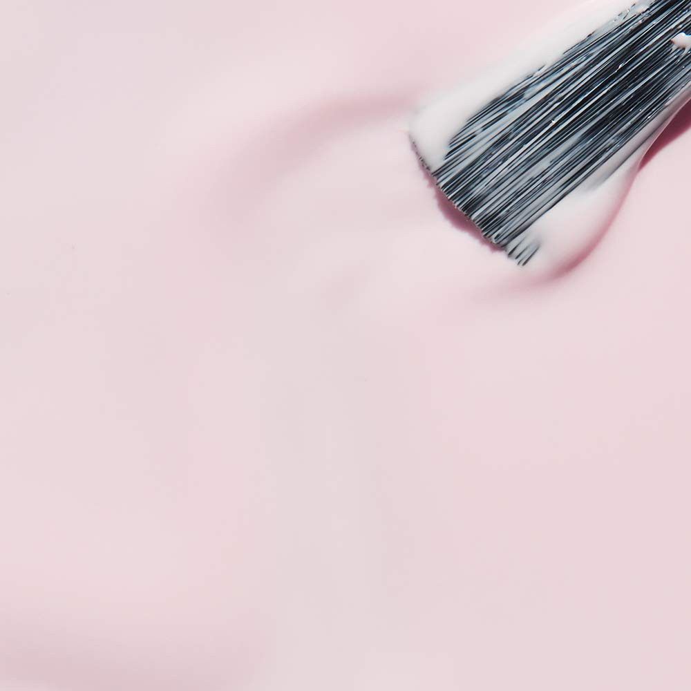 Penseel met roze nagellak. De penseel is bedekt met lak en strijkt over een roze oppervlak.