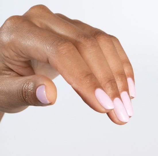 Main avec ongles ovales peints en rose clair. Teint de peau brun moyen. Fond blanc.