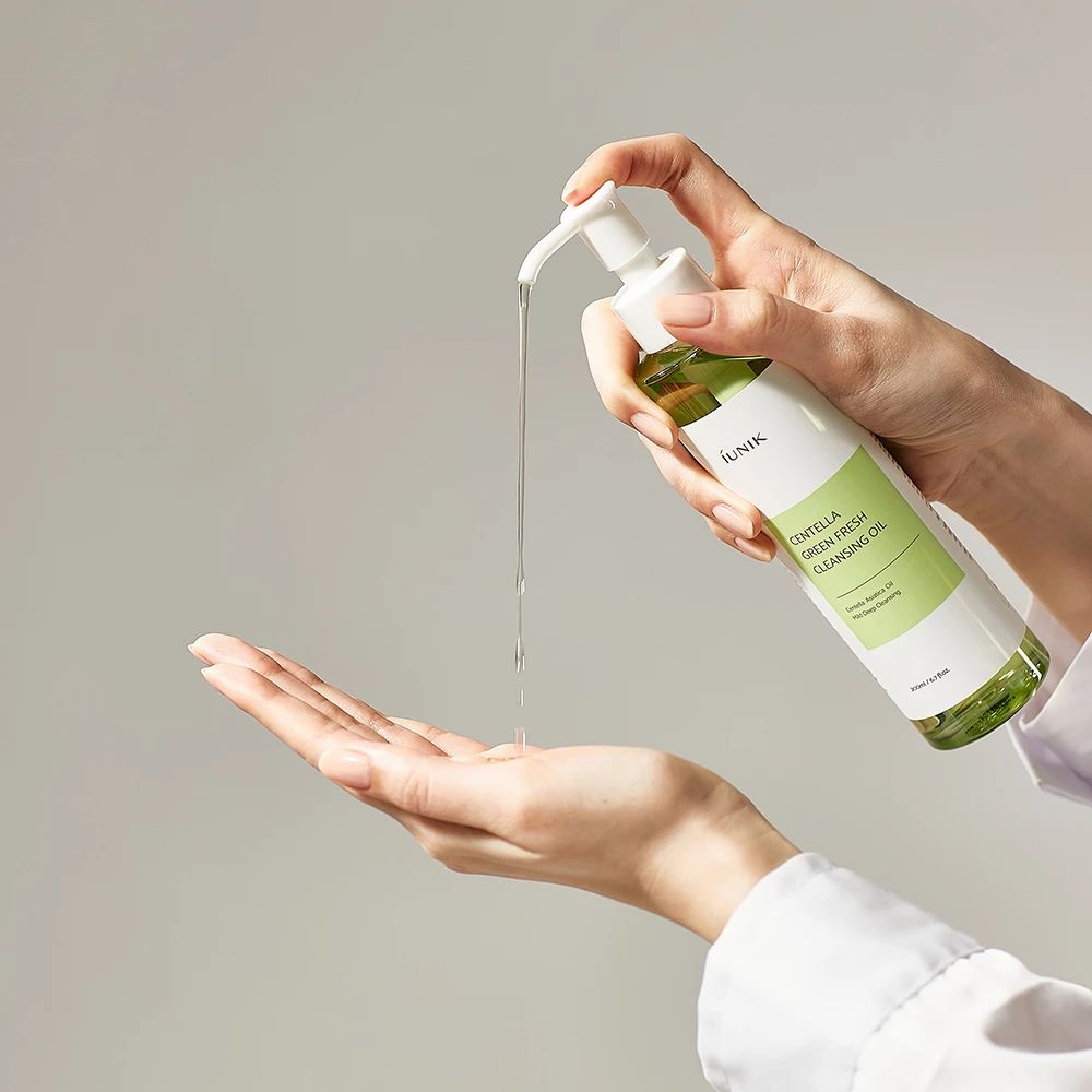 Handen houden een fles vast, olie wordt afgegeven. Opschrift: iUNIK Centella Green Fresh Cleansing Oil.