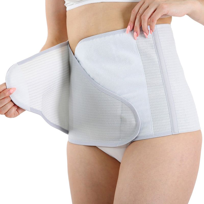 Ceinture abdominale grise à double réglage. Vue latérale, portée par une femme. Fermeture velcro visible.
