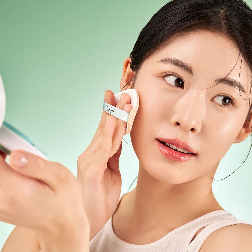 Vrouw die PURITO Centella BB Cushion aanbrengt met een spons. Spiegel op de achtergrond.