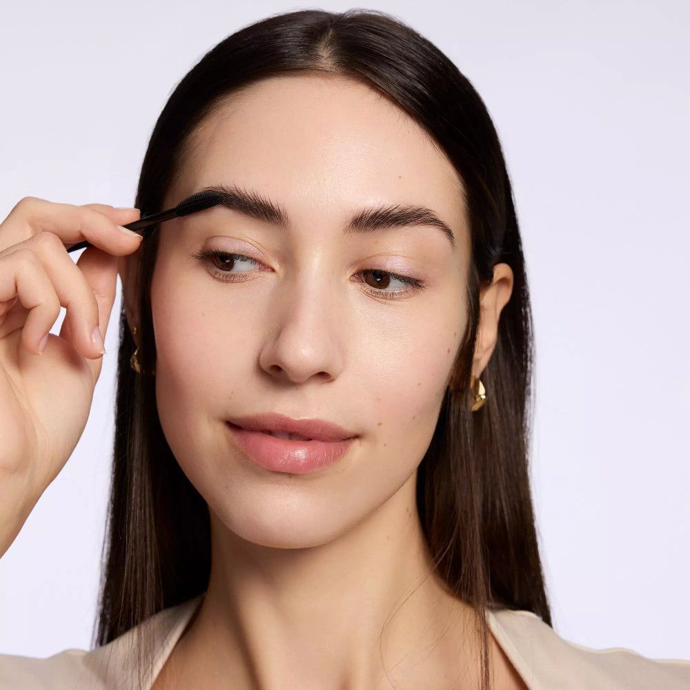 Une femme utilise une brosse à sourcils pour façonner ses sourcils. Elle tient la brosse près de son visage.