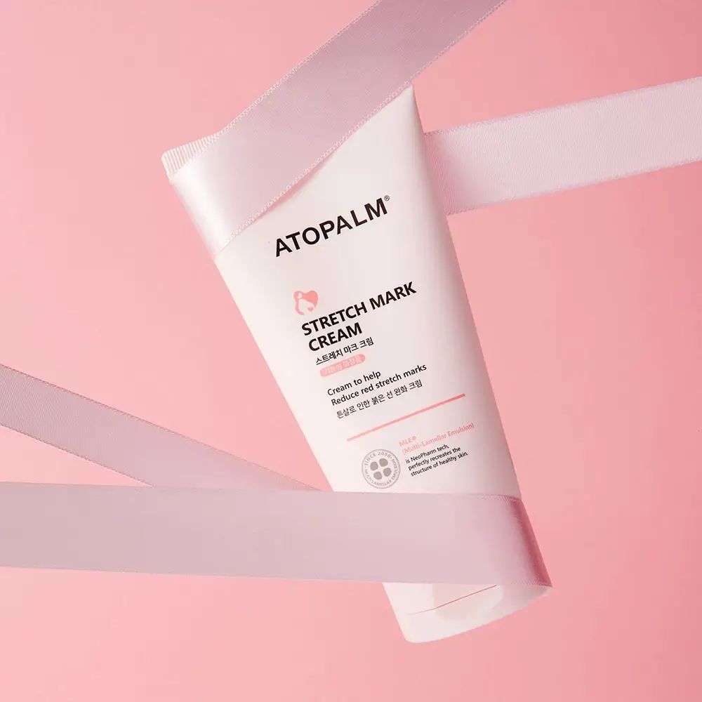 Roze ATOPALM tube en "STRETCH MARK CREAM". Witte linten om de tube op roze achtergrond.