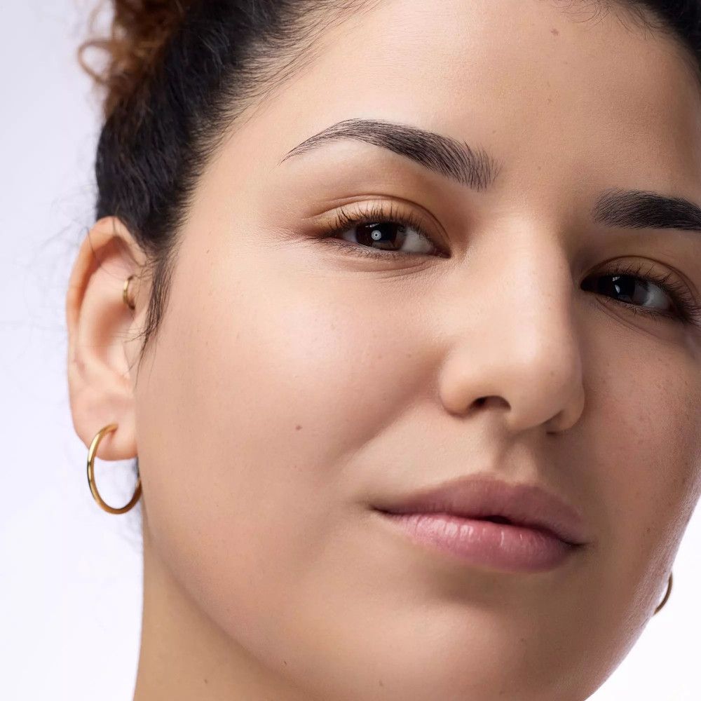 Gros plan sur une femme maquillée. Elle porte des créoles dorées.