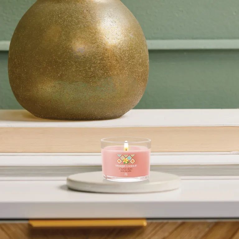 Roze kaars in glazen houder op onderzetter. Opschrift: Capri Glow, Soleil sur Capri. Kaars brandt.