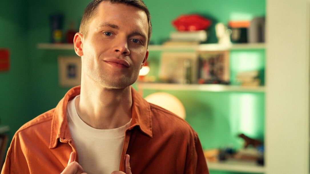 Un homme touche sa poitrine. Il porte une chemise orange et un t-shirt blanc.