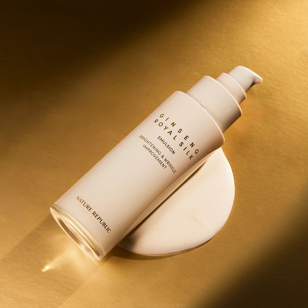 Beige fles met pomp, Ginseng Royal Silk Emulsion. Tekst: Brightening & Wrinkle Improvement. Merk: NATURE REPUBLIC. Op gouden achtergrond.