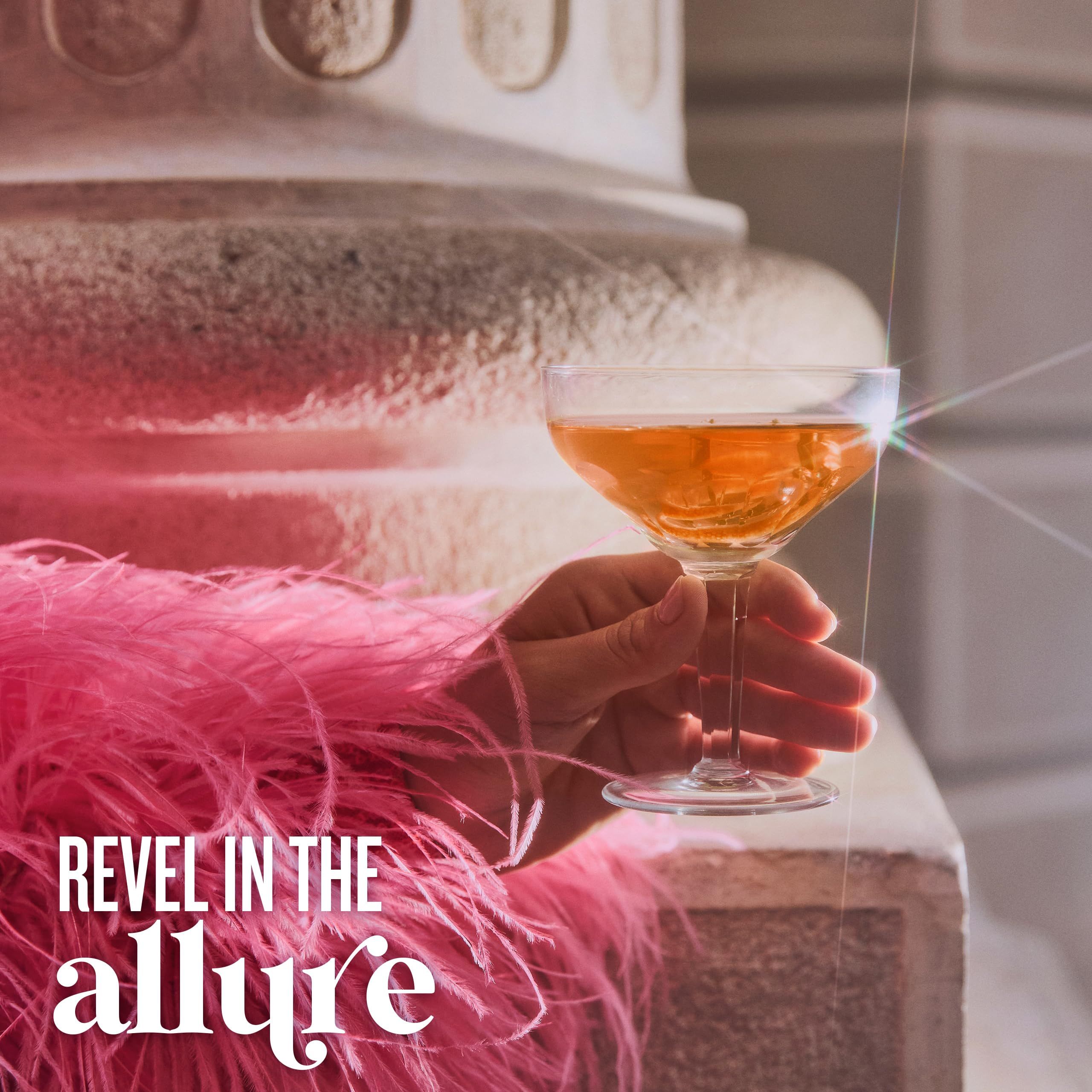 Hand houdt een glas met vloeistof vast. Tekst: Revel in the allure.